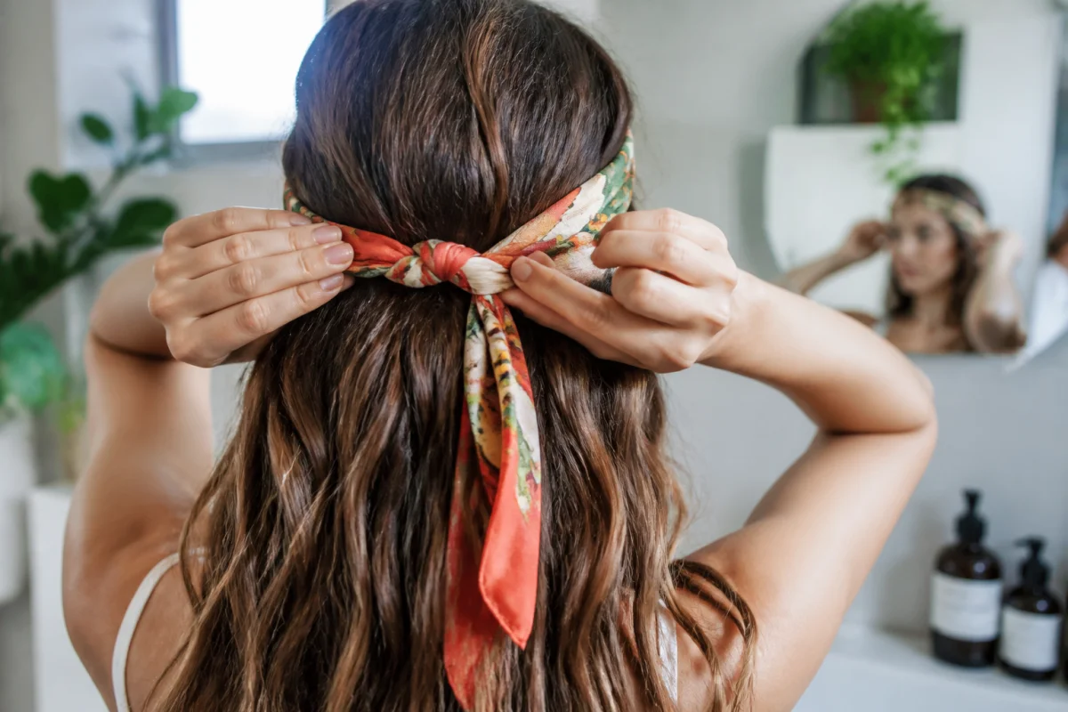 Jeune femme utilisant un ruban coloré pour lisser ses cheveux naturellement dans une salle de bain lumineuse.
